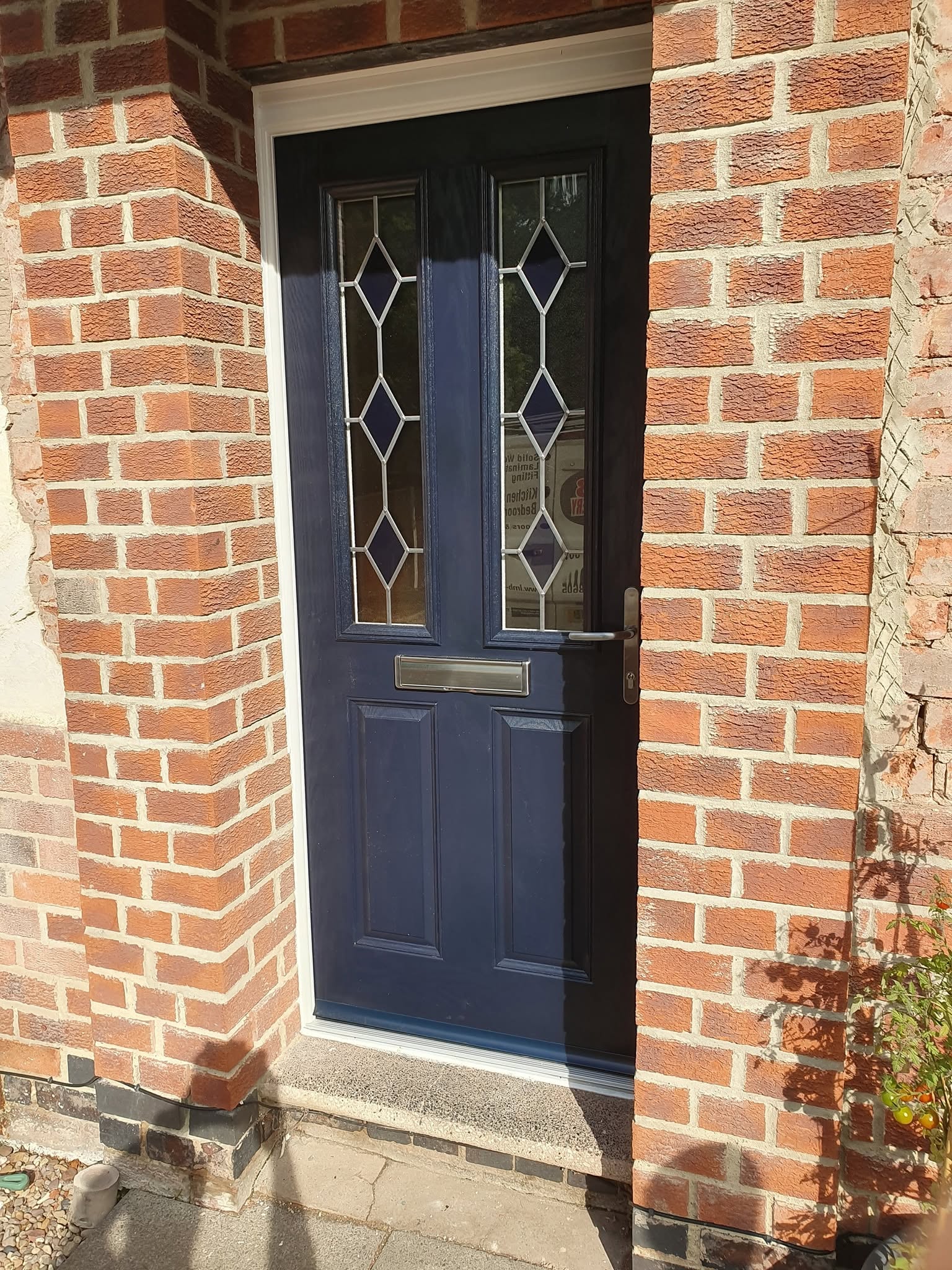 Navy composite front door with leaded diamond glazing fitted into a brick porch by LMB Joinery.