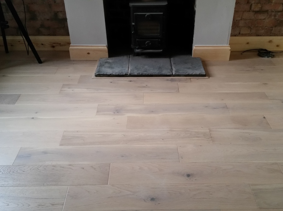 Light oak engineered flooring fitted around a stove with matching skirting boards by LMB Joinery.