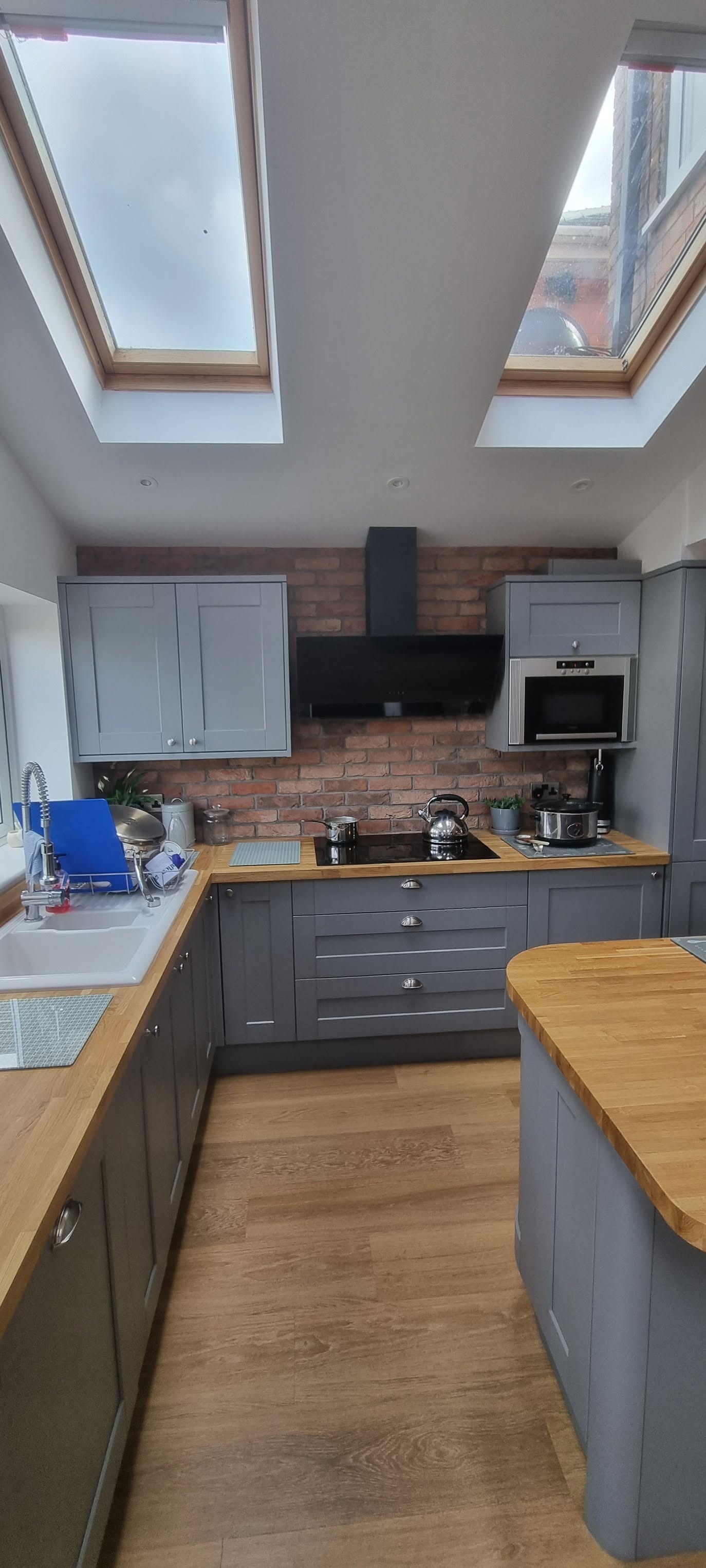 Grey shaker kitchen with solid oak worktops, exposed brick feature wall and Velux windows by LMB Joinery.