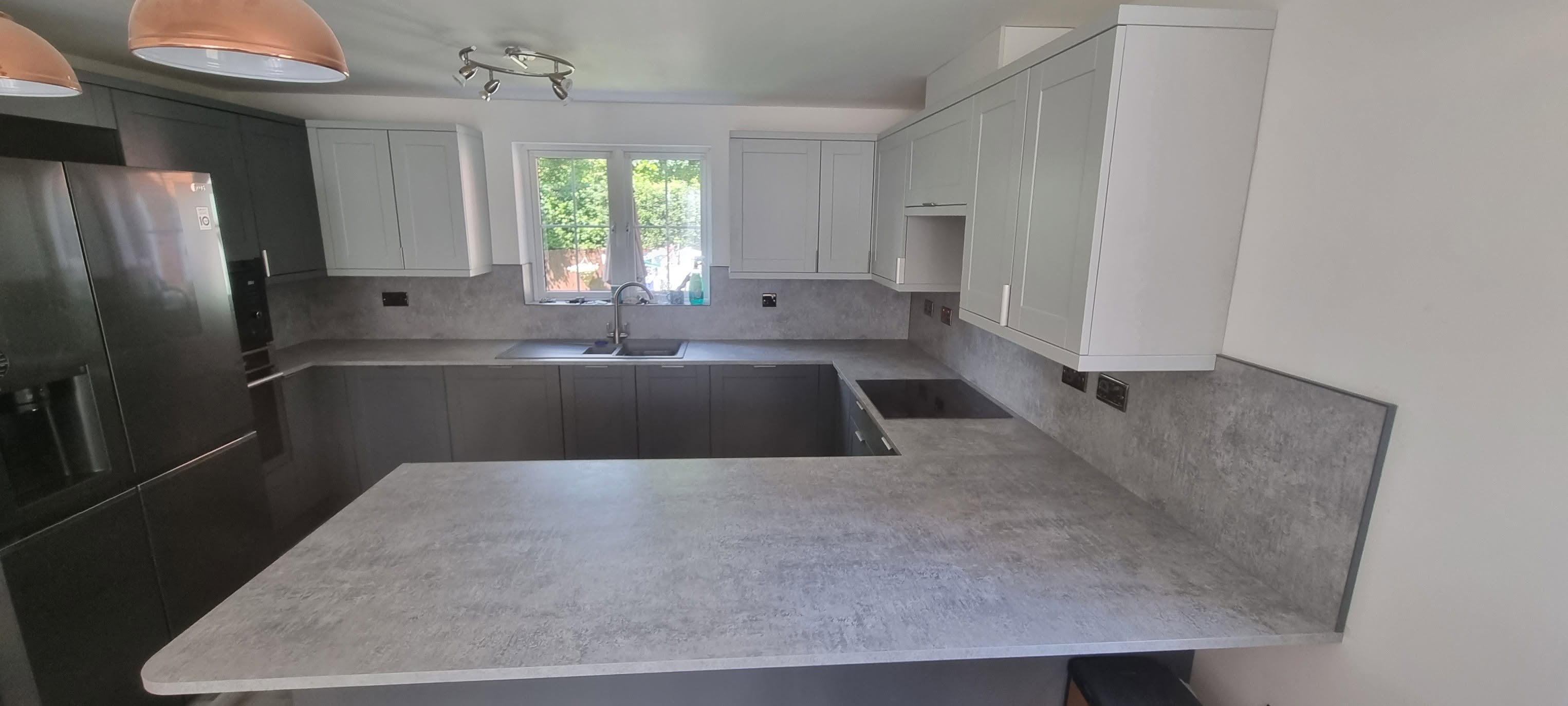 U-shape shaker kitchen in grey and cream with stone-effect worktops and copper pendant lighting by LMB Joinery.